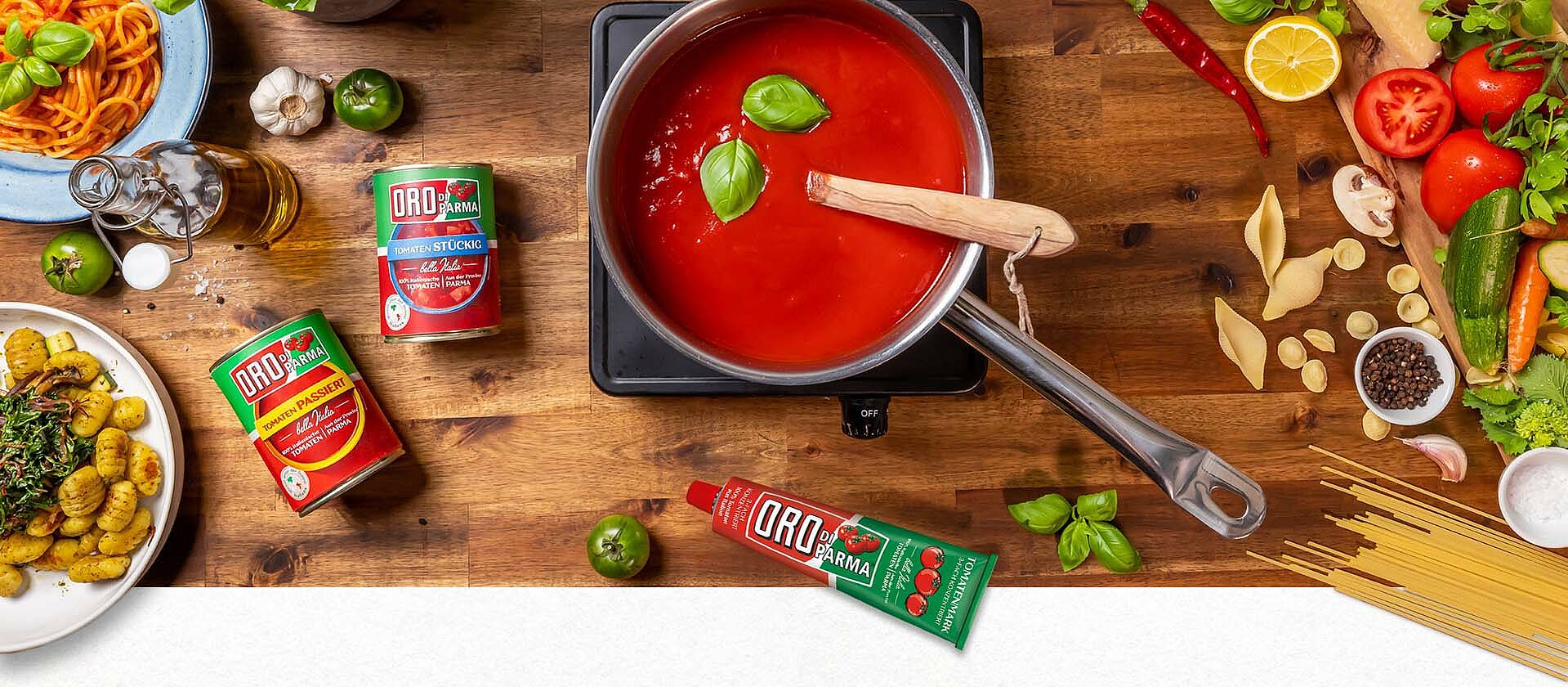 Auf einem Tisch sind verschiedene italienische Gerichte zu sehen. Ebenso ORO di Parma Tomatenprodukte und ein Topf mit selbstgemachter Tomatensauce.